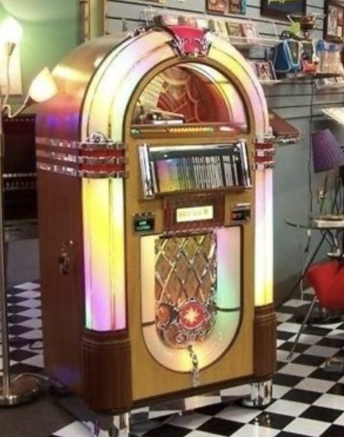 A Wurlitzer 1015 “Bubbler” jukebox lit up on a black-and-white tiled diner floor