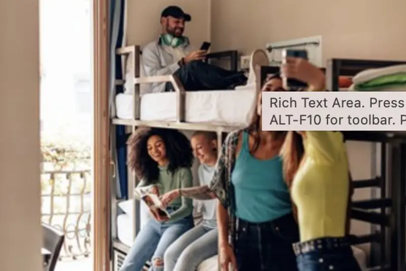 Young travellers talking and taking photographs in a hostel dormitory furnished with bunk beds