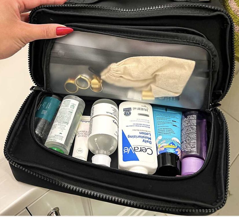 An open toiletries case packed upright with full-size bottles, tubes and jars